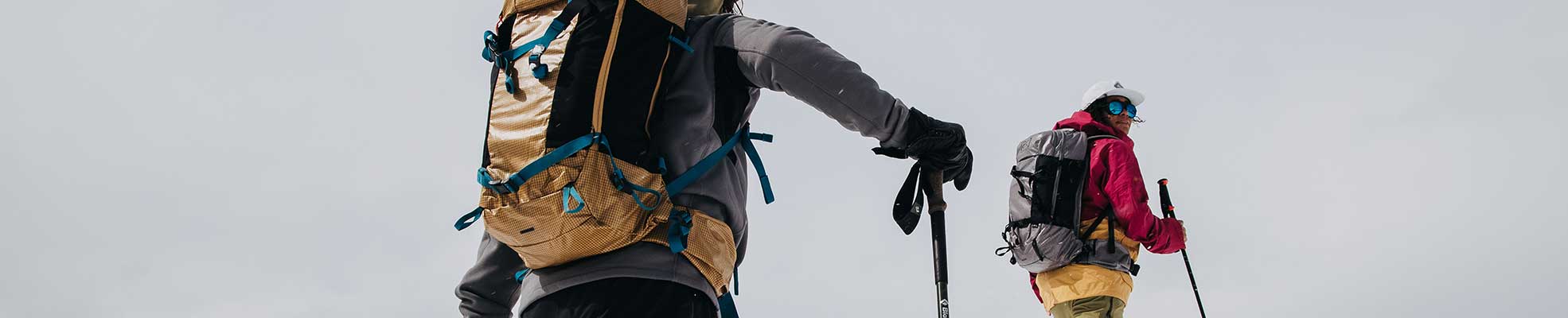 two snowboarders wearing snowboard bags hiking up hill